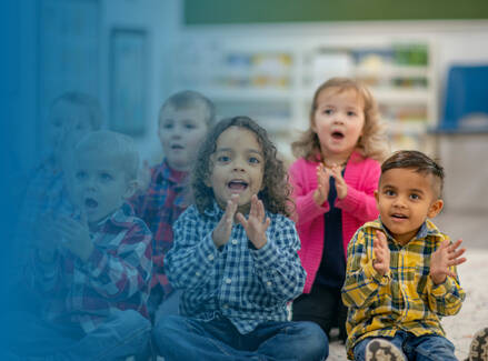 Five children sitting in a classroom excited and clapping